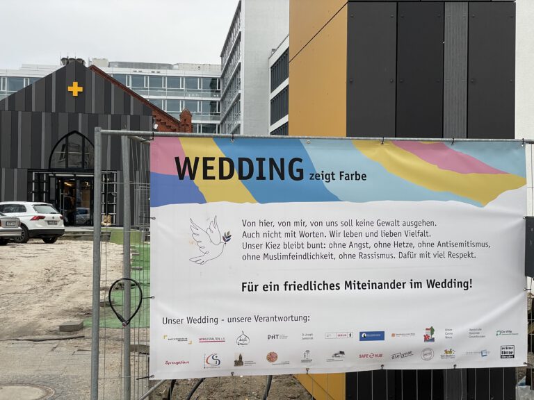 Plakat zur Kampagne "Wedding zeigt Farbe" am Bauzaun vor der Baptistenkirche Wedding.
