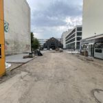 Vor dem Gebäude sind noch von Erde bedeckte Flächen sowie sichtbar, teilweise wurde bereits gepflastert.