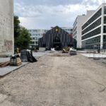 Vor dem Gebäude sind noch von Erde bedeckte Flächen sowie sichtbar, teilweise wurde bereits gepflastert.