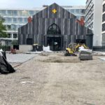 Vor dem Gebäude sind noch von Erde bedeckte Flächen sowie sichtbar, teilweise wurde bereits gepflastert.