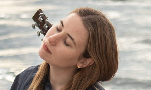 Lina Kahle mit Gitarre auf dem Rücken vor einem Meer.