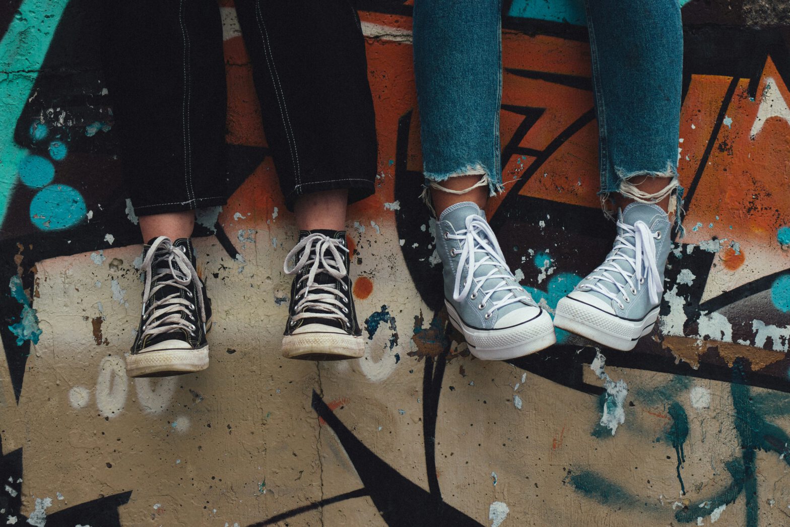 Zwei Beinpaare ab dem Knie sichtbar; Sneaker halbhoch mit weißen Schnürsenkeln.