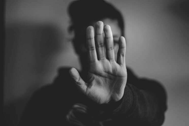 Schwarz-weiß Foto. Mensch hält Hand vor das Gesicht mit einer Stop-Geste.
